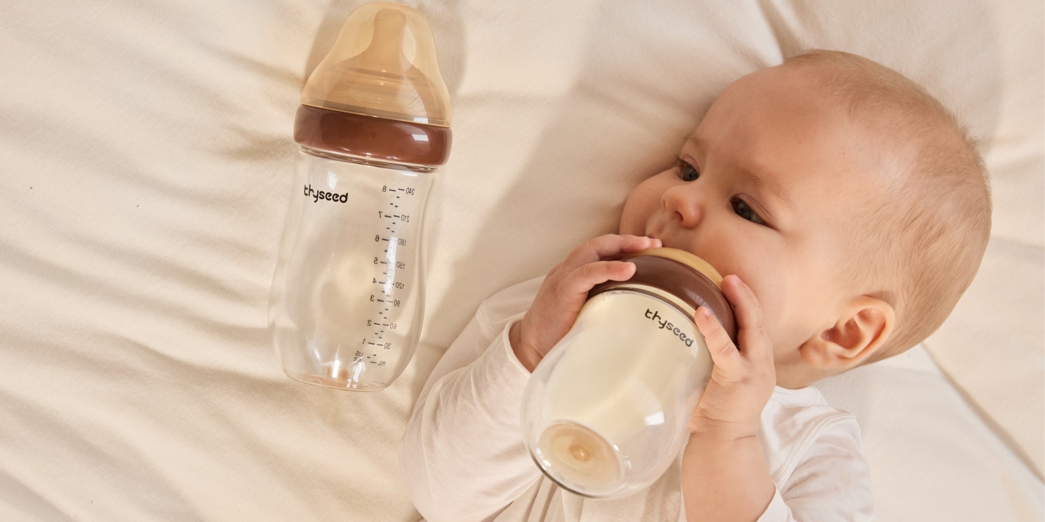Top view of a baby comfortably drinking from a glass anti-colic bottle that prevents air swallowing and gas.