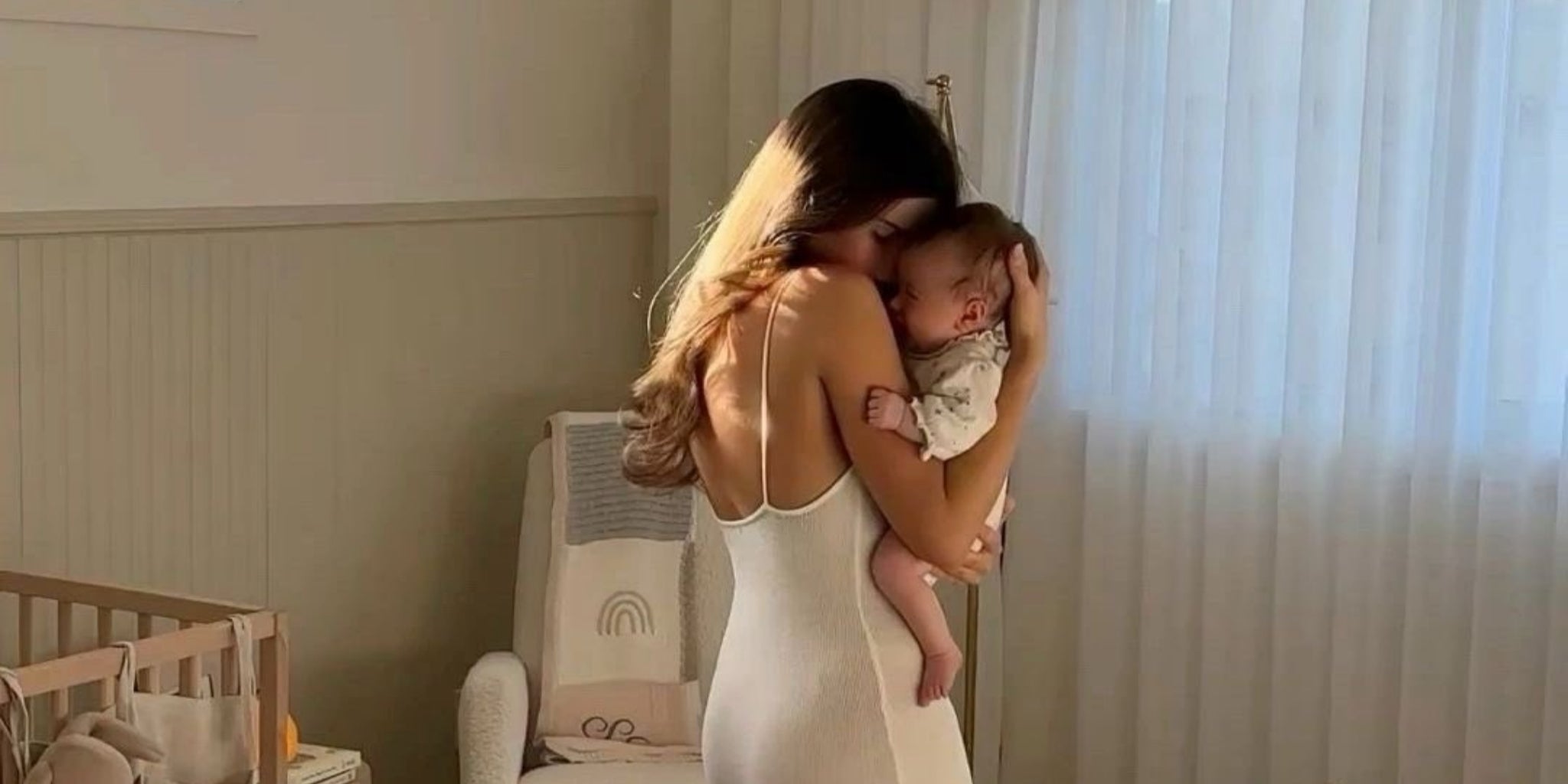A content baby rests peacefully in its mother's arms in a sunlit nursery, satisfied after a bottle feeding.