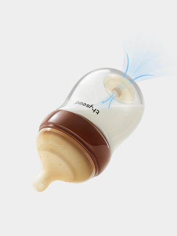Thyseed glass anti-colic baby bottle with brown collar and beige nipple, showing airflow through the vent.